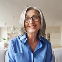 Untitled design (7) Older white woman sitting and smiling.