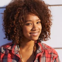 Untitled design (9) lady with afro hair smiling wear a checked shirt