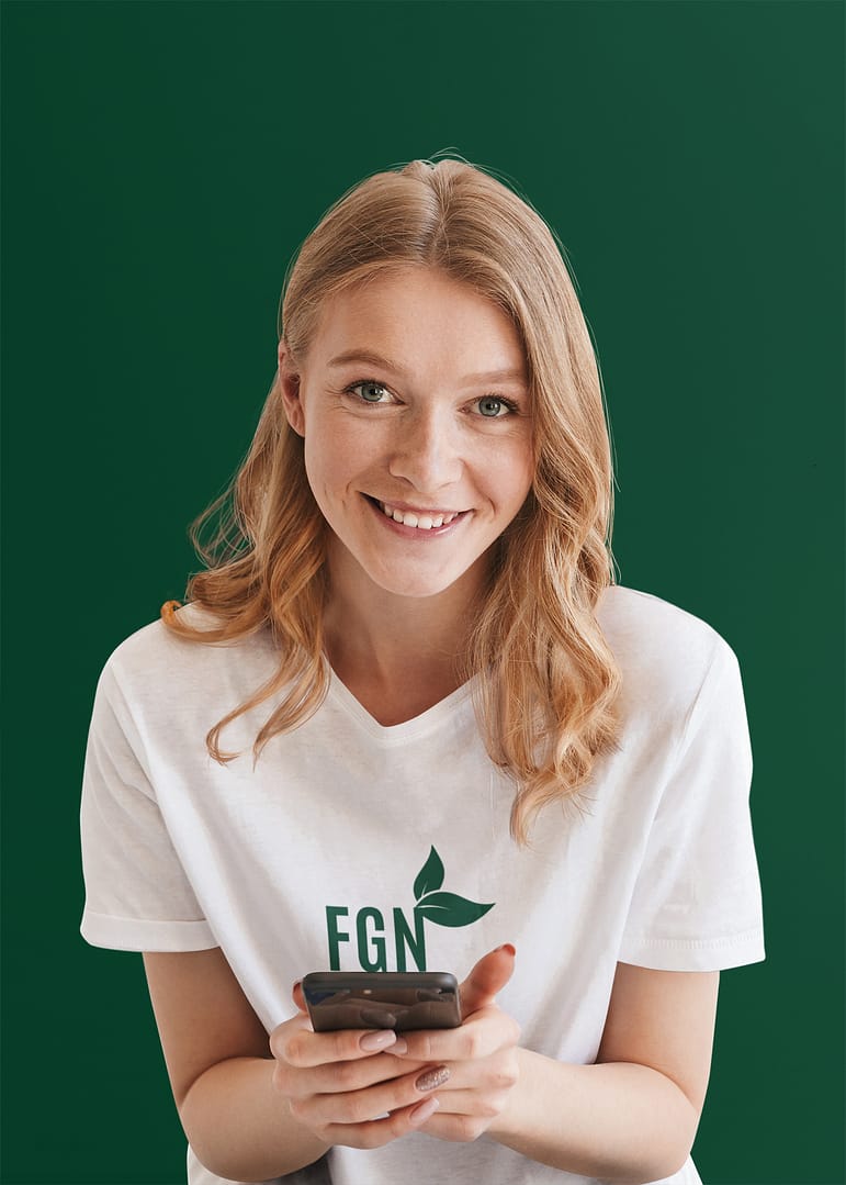 t-shirt-mockup-of-a-woman-holding-a-phone-in-a-studio-38201-r-el2 Young adult wearing white T-shirt with logo and holding a phone.